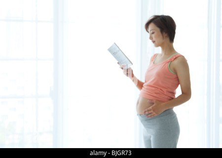 Pregnant woman standing and reading a book by the window Stock Photo