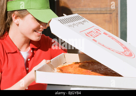 Woman in sun visor looking into opened pizza box - Stock Photo