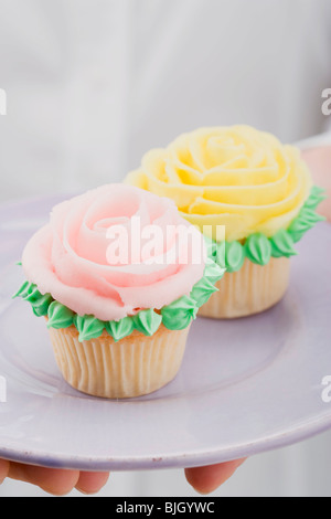 Hands holding two cupcakes with marzipan roses on plate - Stock Photo