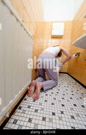 Young woman (32 years), feeling sick, kneeling in pyjamas in front of the toilet Stock Photo