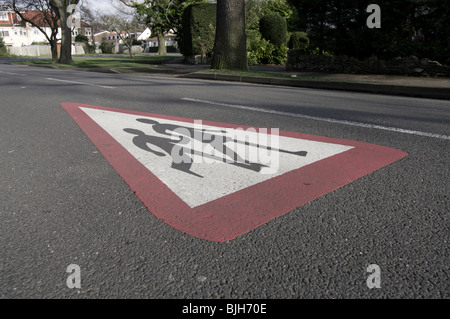 Children crossing warning pained on road showing 2 schoolchildren holding hands as a warning to drivers Stock Photo