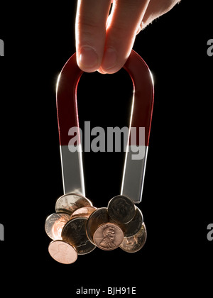 hand holding a magnet with a bunch of coins stuck to it Stock Photo