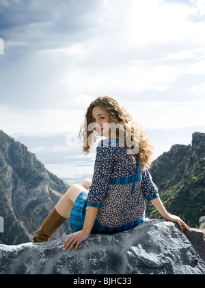 woman in a floral print dress on a mountain top sitting on a rock Stock Photo