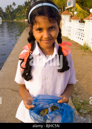 India, Kerala, Alappuzha, Chennamkary, backwaters, young girl showing fish caught in shallows near riverbank Stock Photo