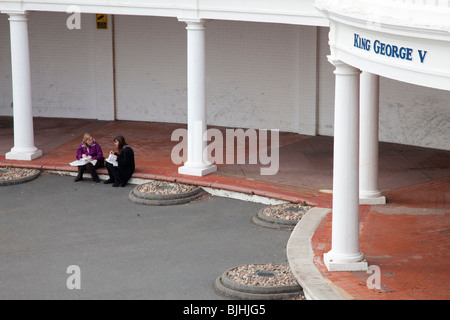 Two women eating a lunch of fish and chips from paper on the prom below the Pavilion at Bexhill, East Sussex, UK Stock Photo