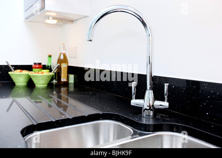 High key close up image of a modern kitchen interior with the main focus on the chrome tap and granite worktop.