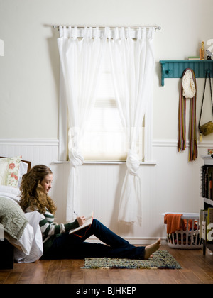 young woman sitting on the floor in her bedroom writing in a journal Stock Photo