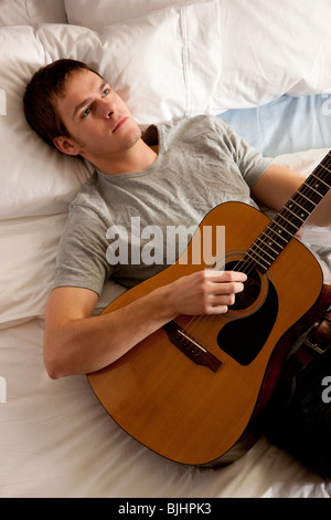 man lying in bed with his guitar Stock Photo