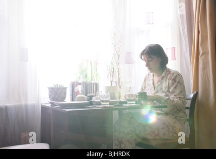 Woman sitting at morning breakfast table by window Stock Photo
