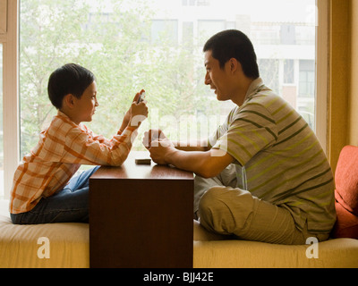 Profile of man and boy sitting cross legged in front of large window playing cards Stock Photo