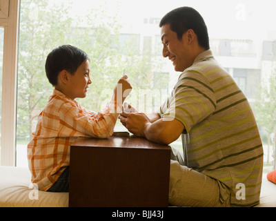 Profile of man and boy sitting cross legged in front of large window playing cards Stock Photo