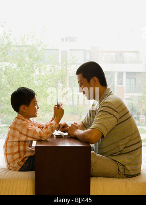 Profile of man and boy sitting cross legged in front of large window playing cards Stock Photo