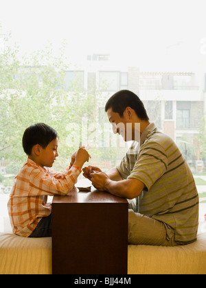 Profile of man and boy sitting cross legged in front of large window playing cards Stock Photo