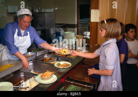 England, East Sussex, Brighton, Young girl collecting her hot meal from dinner lady at counter in school canteen.