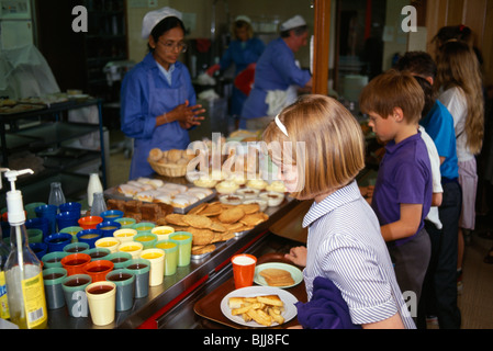 England, East Sussex, Brighton, Young girl collecting her hot meal from dinner lady at counter in school canteen.