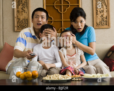 Family watching television with parents covering children's eyes Stock Photo