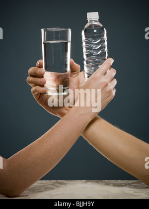Hand holding glass of water and hand holding bottled water intertwined Stock Photo