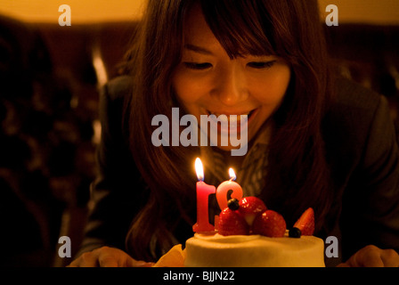 Woman leaning over to blow out the candles on her birthday cake Stock Photo