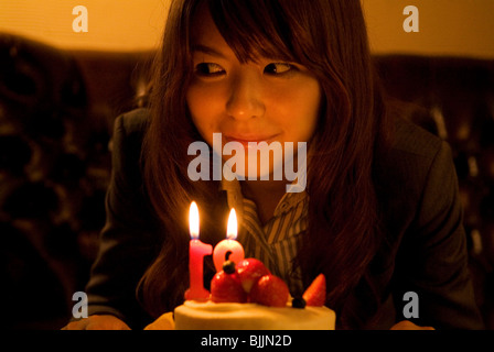 Woman leaning over to blow out the candles on her birthday cake Stock Photo