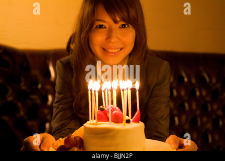 Woman leaning over to blow out the candles on her birthday cake Stock Photo