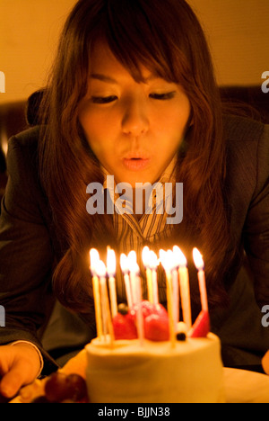 Woman leaning over to blow out the candles on her birthday cake Stock Photo