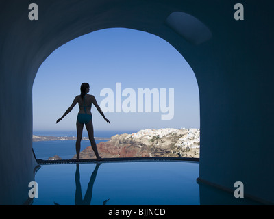 Woman in swimsuit standing at edge of infinity pool rear view Stock Photo