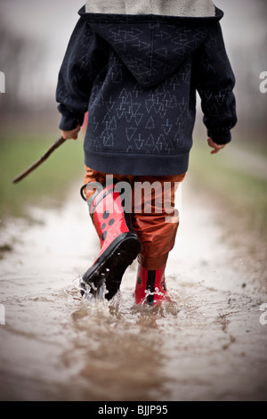 Young boy wearing rain boots walks through a puddle of water. Stock Photo