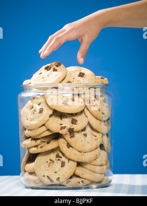 Hand grabbing chocolate chip cookie from jar Stock Photo