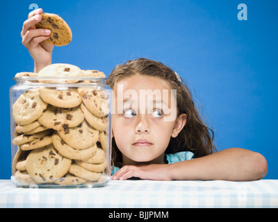 Girl taking chocolate chip cookie from jar Stock Photo