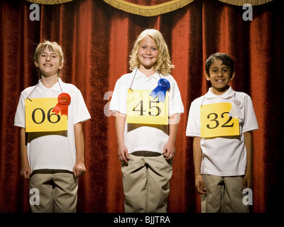 Three children on stage at winner's podium with ribbons smiling Stock Photo