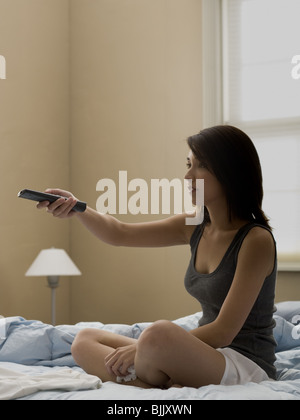 Woman sitting on bed with television remote and tissue Stock Photo