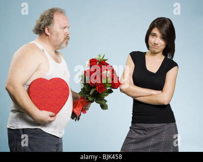 Disheveled man with heart box and red roses with disinterested woman Stock Photo