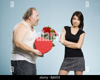 Disheveled man with heart box and red roses with disinterested woman Stock Photo