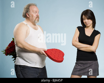 Disheveled man with heart box and red roses with disinterested woman Stock Photo