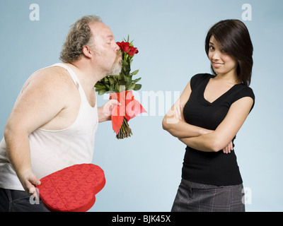 Disheveled man with heart box and red roses with disinterested woman Stock Photo