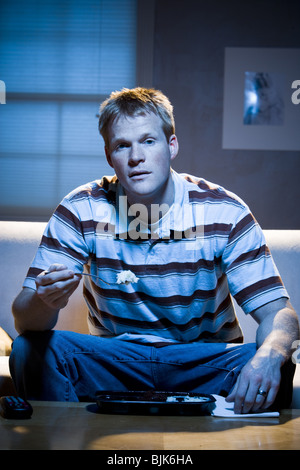 Man on sofa with frozen dinner and napkin with food Stock Photo