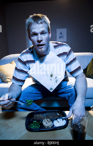 Man on sofa with frozen dinner and napkin with food Stock Photo