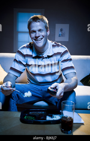 Man on sofa with frozen dinner and napkin with food smiling Stock Photo