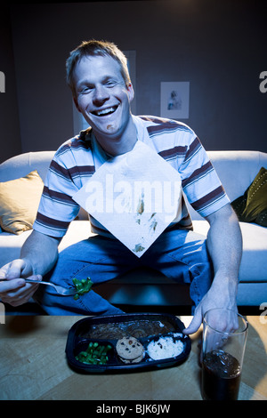 Man on sofa with frozen dinner and napkin with food smiling Stock Photo