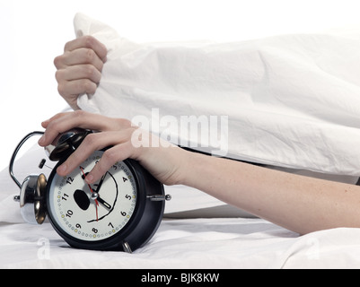 young woman woman in bed awakening tired holding alarm clock on white background Stock Photo