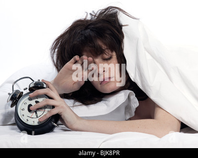 young woman woman in bed awakening tired holding alarm clock on white background Stock Photo