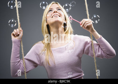 Woman blowing bubbles on swing Stock Photo