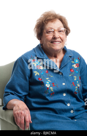 Elderly woman sitting in an armchair and smiling isolated on white ...