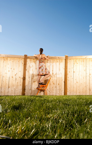 Woman standing on chair peeping over fence Stock Photo - Alamy