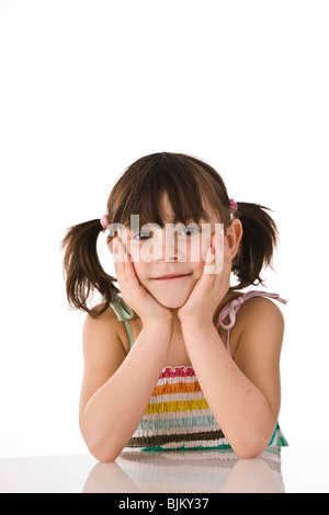 Girl with pigtails sitting at a table leaning on her hands Stock Photo