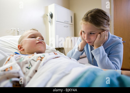Young girl sitting by brother in hospital bed Stock Photo