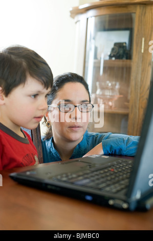 Four and 1/2 year old Hispanic boy surfs the internet on his laptop at home with the help of his mother. Model Released. Stock Photo