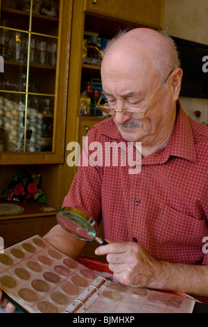 Pensioner looking at his coin collection with a magnifying glass Stock Photo