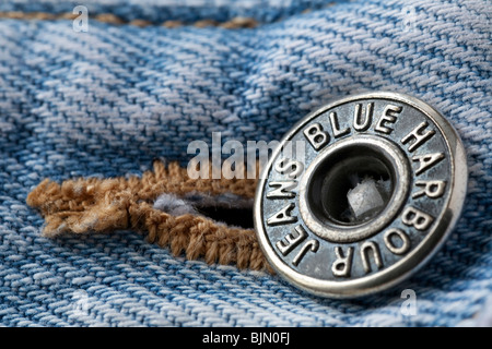 Close up image of the metal waist band fastening on a pair of faded blue denim jeans showing the makers brand name Stock Photo