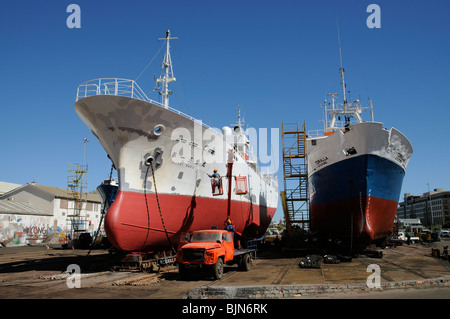 Man in cherry picker painting the hull of a fishing vessel in a dockyard Port of Cape Town South Africa Stock Photo